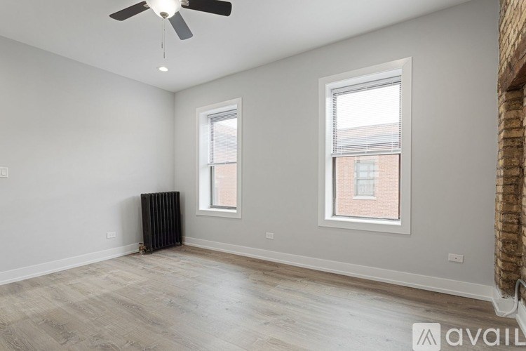 A room with a fan, two windows, and a radiator.