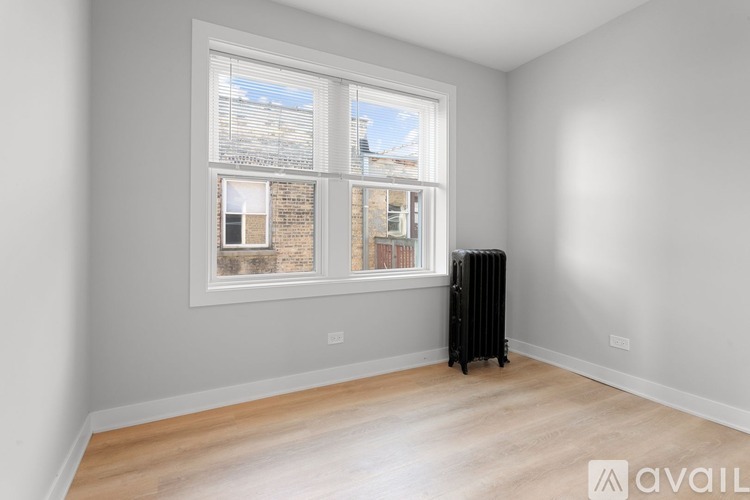 A room with a window overlooking a brick building and a radiator on the floor.