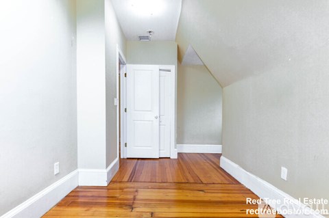 A hallway with a white door and wooden floors.