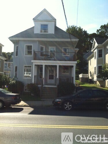 A white house with a balcony is on the corner of a street.