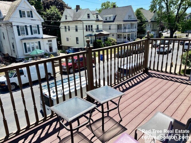 A wooden deck with a table and chairs overlooks a street with parked cars.