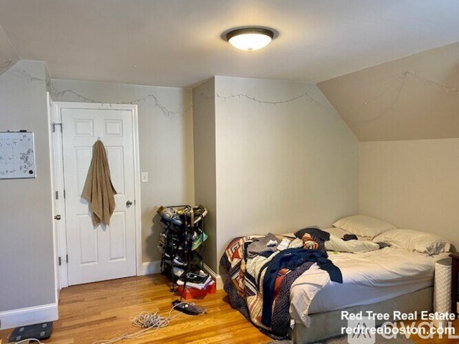 A bedroom with a bed, a coat hanging on the door, and a white wall.