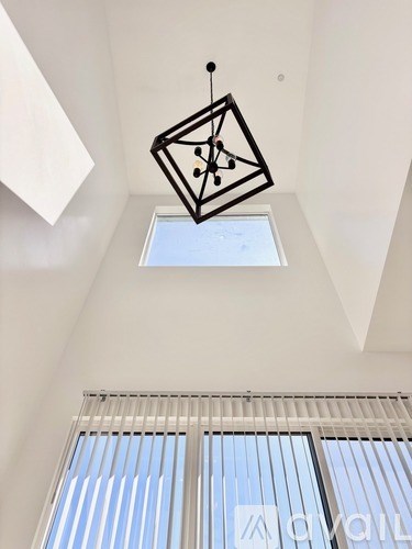 A geometric hanging sculpture in a white room with a skylight.