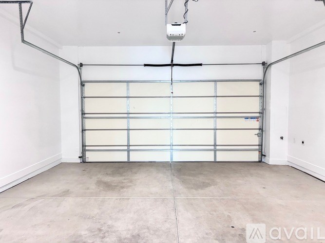 A large, empty garage with a roll-up door and a ceiling fan.