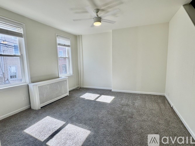 A room with a carpet floor, a window, and a ceiling fan.