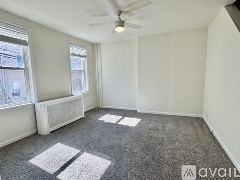 A room with a carpet floor, a window, and a ceiling fan.