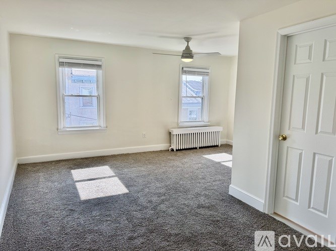 A room with a carpeted floor, two windows, and a door.
