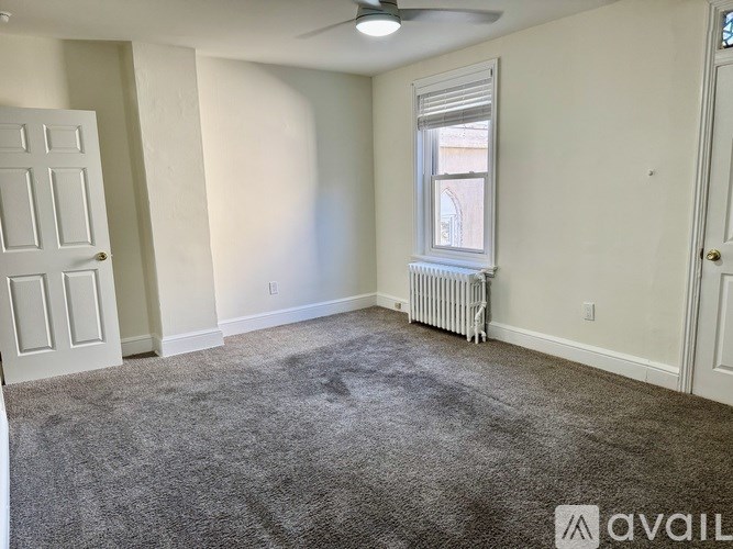 A room with a carpeted floor, a window with blinds, and a ceiling fan.