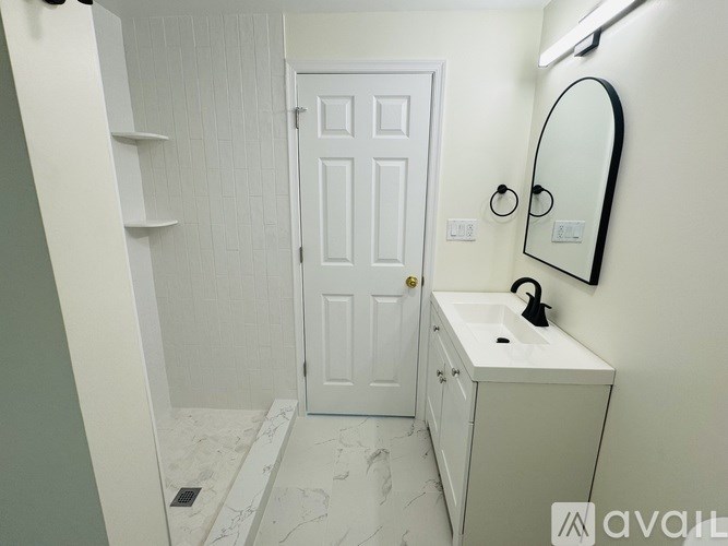 A bathroom with a white door, sink, and mirror.