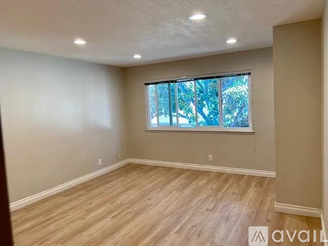 A room with wooden flooring and a window with a view of trees.