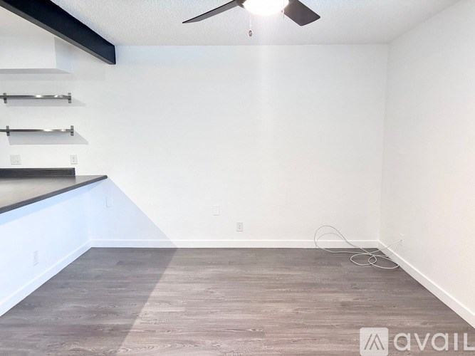 A room with a fan and a wooden floor.