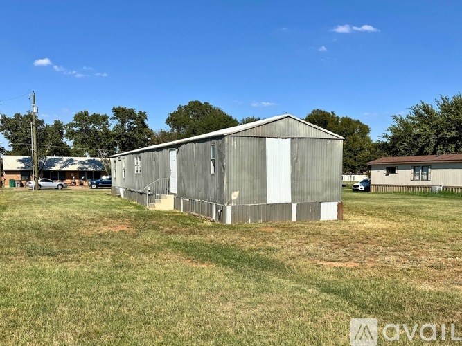 A large, grey metal building sits in a grassy field.