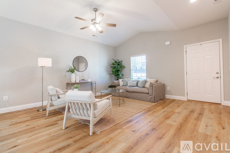 A living room with a white chair, a grey couch, a floor lamp, a small potted plant, and a round mirror on the wall.
