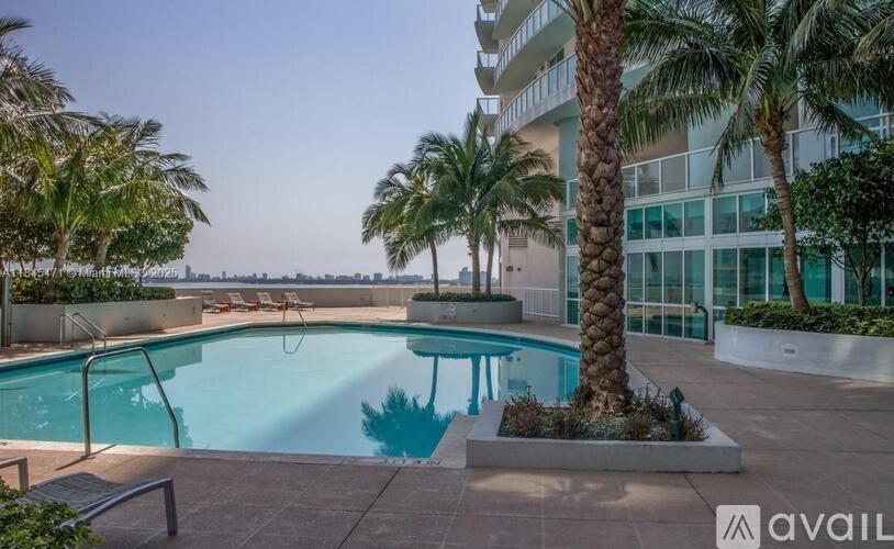 A pool surrounded by palm trees and a building in the background.
