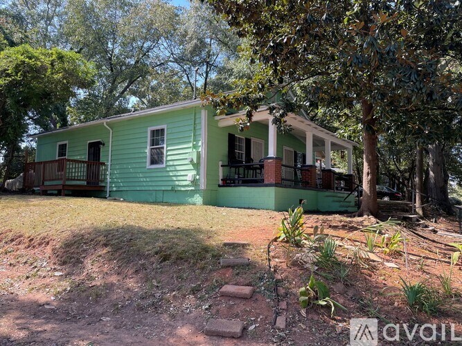 A green house with a white porch and a tree in front.