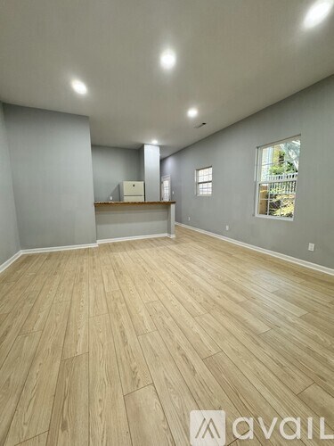 A room with wooden flooring and a window showing a fence and trees outside.