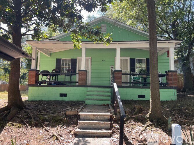 A green house with a porch and a tree in front.