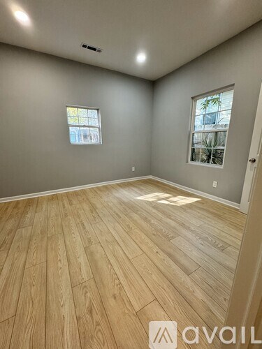 A room with wooden flooring and two windows.