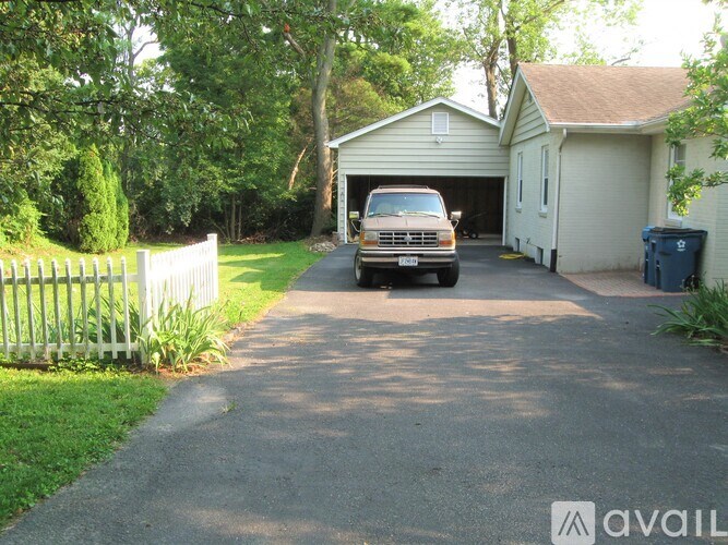 A white picket fence and a green trash can are on the left side of a driveway.
