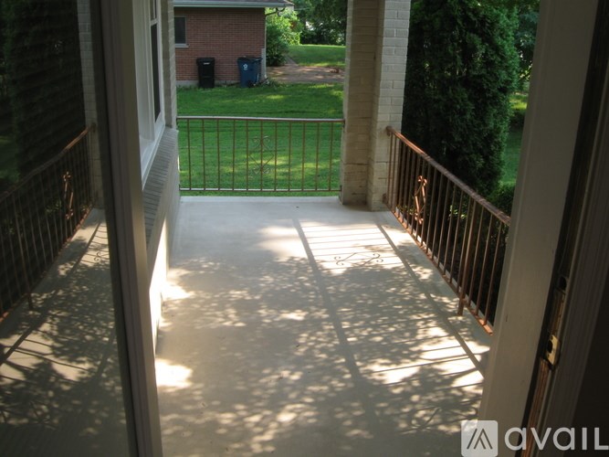 A balcony with a metal railing and a view of a green lawn and a house.