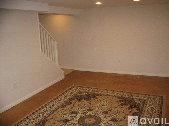 A room with a patterned rug on the floor and a stairwell to the left.