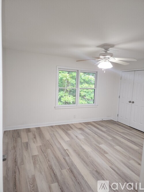 A room with a ceiling fan and a window overlooking trees.