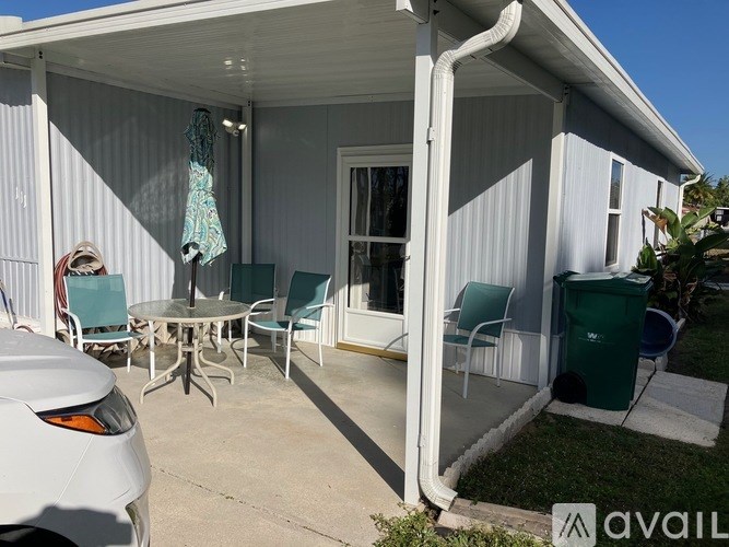 A white car is parked in front of a house with a patio.