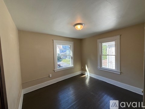 A room with two windows and wooden floors is available for rent.