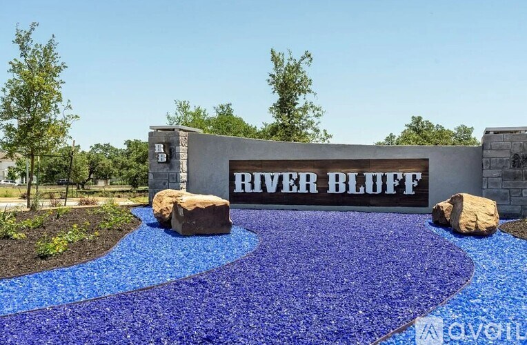 A blue pebble-covered walkway leads to a building with the name River Bluff on it.