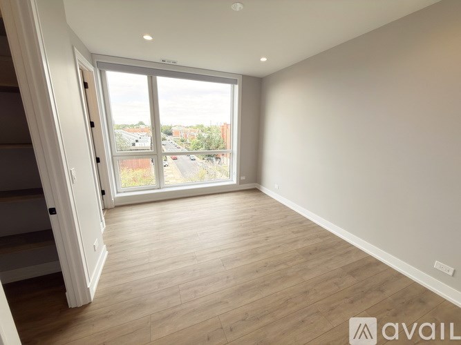 A spacious room with wooden flooring and a large window overlooking a street.