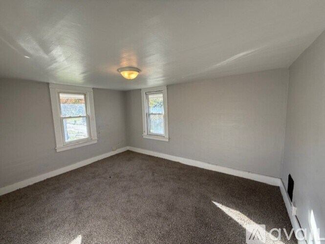 A room with a carpeted floor and two windows.