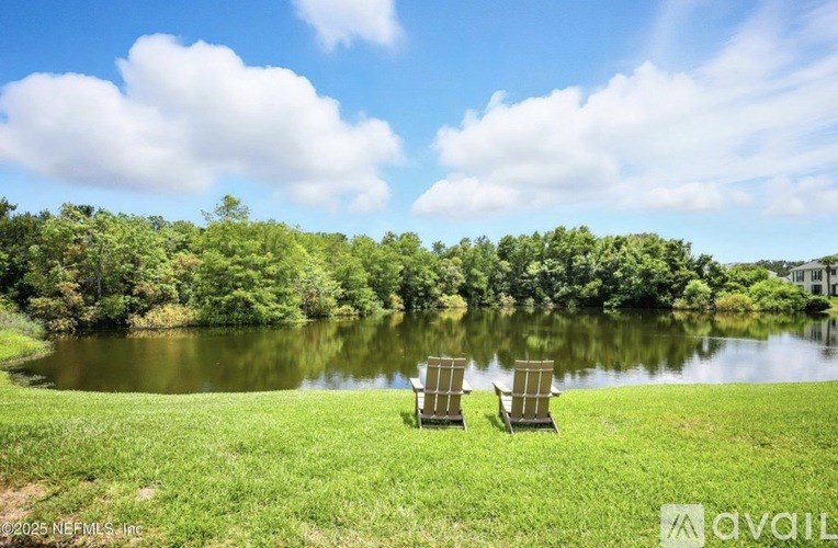 Two lawn chairs are placed on a grassy area in front of a lake.