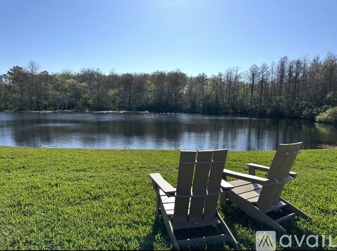 Two adirondack chairs are placed on a grassy area near a lake.