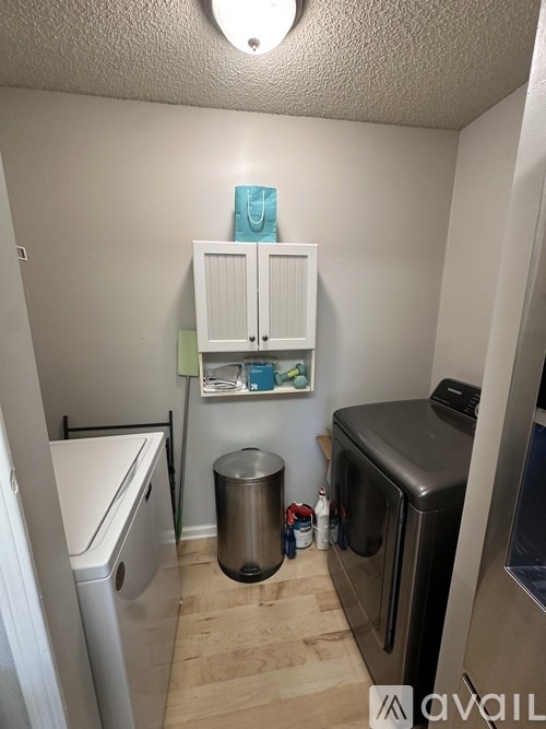 A small kitchen with a white fridge, a white dishwasher, a white cabinet with a blue bag on top, a black trash can, and a black oven.