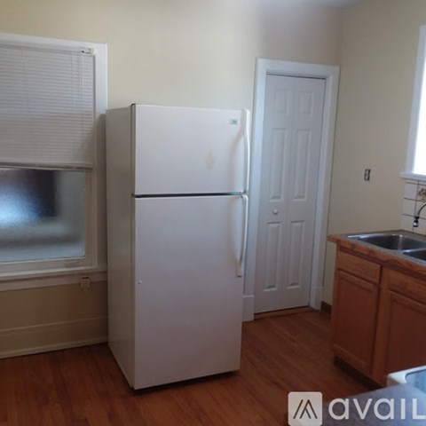 A white refrigerator in a kitchen with wooden floors and a white door.