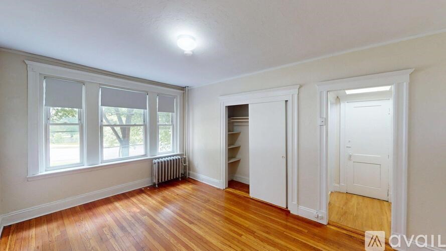 A room with wooden floors and white walls, featuring a window with a view of trees outside.