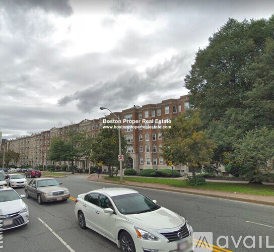 A white car is driving down a street with other cars parked on the side.