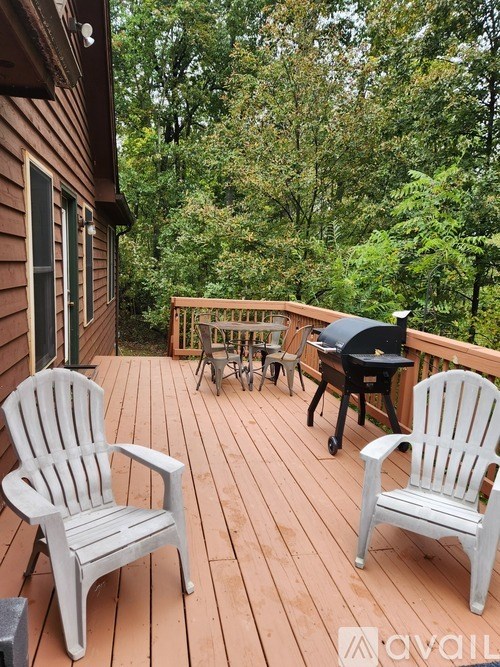 Two chairs are on a wooden deck with a grill and table.