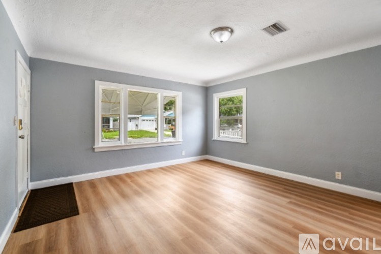 A room with wooden flooring and two windows with pictures on the wall.