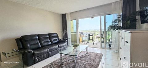 A living room with a black leather sofa and a glass table.