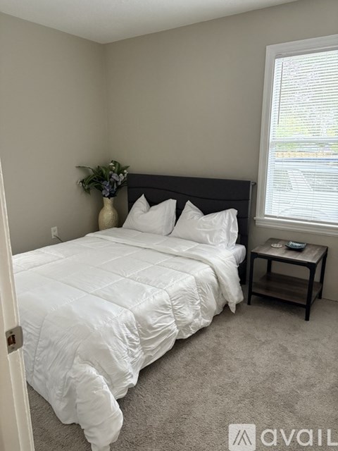 A bedroom with a white bed and a small table with a vase of flowers on it.