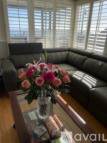 A vase of pink roses sits on a coffee table in front of a grey sofa.