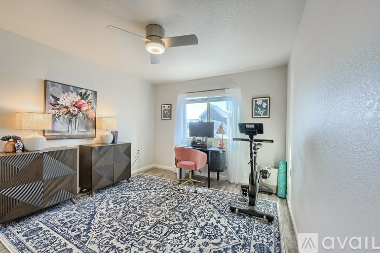 A room with a rug, a fan, a chair, and a table.