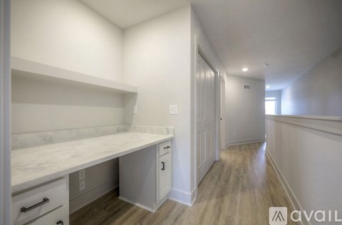 A white kitchen with a marble counter top and wooden floors.