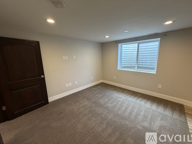 A room with a carpeted floor, a window with blinds, and a wooden door.