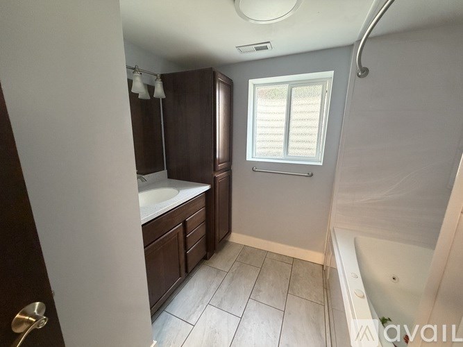 A bathroom with a white tub and a window with blinds.
