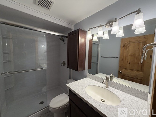 A bathroom with a toilet, sink, mirror, and shower.