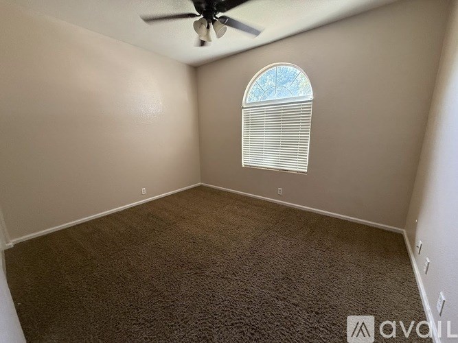 A room with a carpeted floor, a ceiling fan, and a window with blinds.