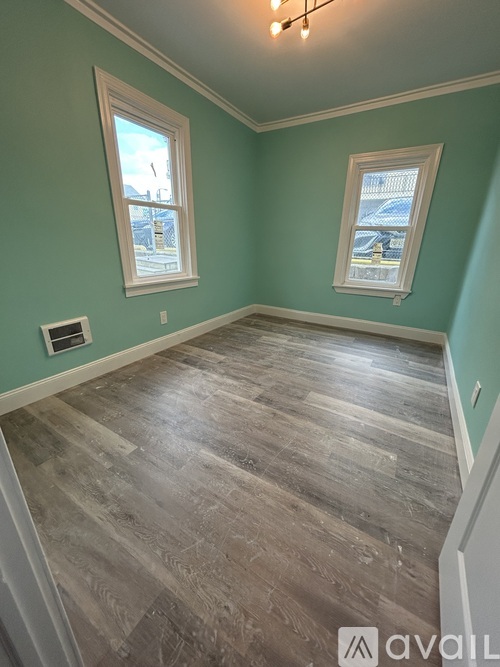A room with wooden flooring and two windows.