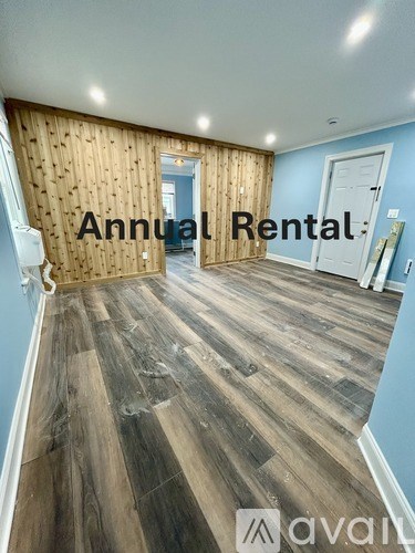 A room with wooden flooring and a wall covered in wood planks with the text "Annual Rental" and "avail" written on it.